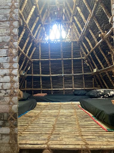Non-AC Dorm — long thatched interior with multiple beds